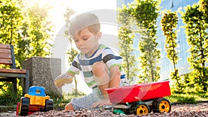 Closeup portrait of happy smiling 3 years old child boy digging sand on the playground with toy plastic truck or