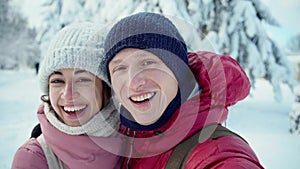 Closeup portrait of happy smiling young couple kissing and hugging while walking in snowy winter park at sunny winter