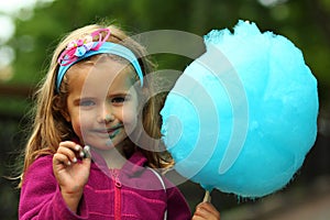 Closeup portrait of happy toddler girl eating blue cotton candy