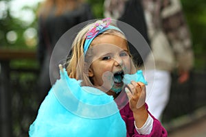 Closeup portrait of happy toddler girl eating blue cotton candy