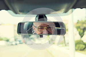 Closeup portrait, happy young man driver looking at rear view mirror smiling