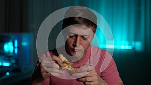 Closeup portrait of hungry man dipping slice of pizza in sauce sitting at table in evening or night on blurred