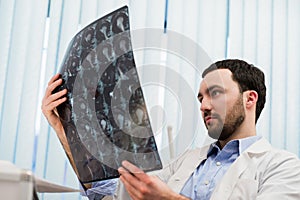 Closeup portrait of intellectual man healthcare personnel with white labcoat, looking at brain x-ray radiographic image