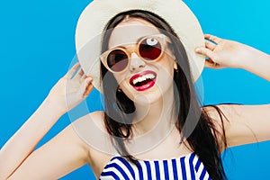 Closeup Portrait of Laughing Female Model in Fashion Sunglasses and Summer Hat on Blue Background.