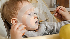 Closeup portrait of little baby boy getting messy while mother is feeding him from spoon. Concept of parenting, healthy nutrition