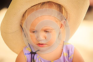 Closeup Portrait of Little Blond Girl in Hat against Sand