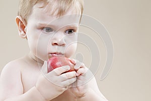 Closeup Portrait of Little Caucasian Child With Red Apple Fruit in Hands While Eating And Posing Against Beige Background