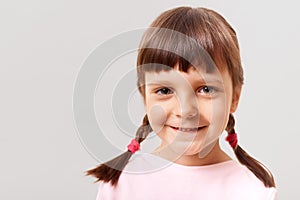 Closeup portrait of little cute girl indoors, child looking at camera with a happy smile, a positive girl with pigtails, dressed