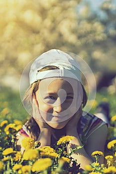 Closeup portrait of little cute girl lying with dandelions on the grass. Happy smiling girl lies on the grass among