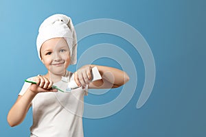 Closeup portrait of a little girl on a blue background. The child brushes his teeth and squeezes the toothpaste onto the