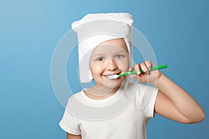 Closeup portrait of a little girl on a blue background. A child with a white towel on his head brushing his teeth.