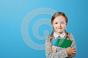 Closeup portrait of a little girl schoolgirl on a blue background. The child holds books. The concept of education and school.