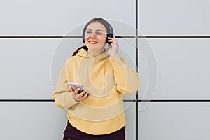 Closeup portrait of a lovely young girl listening to music through wireless earphones and singing on gray background