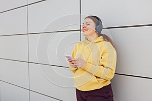 Closeup portrait of a lovely young girl listening to music through wireless earphones and singing on gray background