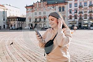 Closeup portrait of a lovely young girl listening to music through wireless earphones on urban background. Music lover