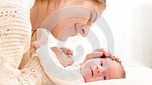 Closeup portrait of loving young mother stroking her 1 months old baby boy lying on bed. Concept of family happiness and