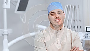 Closeup portrait male dentist in medical uniform smiling posing with crossed hands at operating room