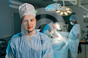 Closeup portrait of male doctor in surgical uniforms standing posing looking at camera in dark modern operating room.