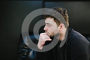 Closeup portrait of a man with hearing aid on a dark background, looking away with a serious face. Handsome bad-hearing guy sits