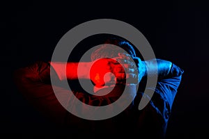 Closeup portrait of man in neon light. Human emotions, facial expressions, headaches, reflections on the past. holds his hands