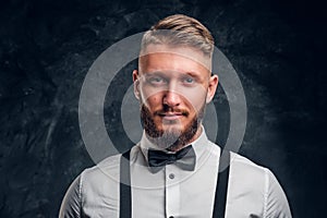 Closeup portrait of a man with stylish beard and hair in shirt with bow tie and suspenders. Studio photo against dark