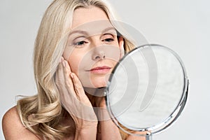 Closeup portrait middle age 50 woman looking at mirror, touching healthy skin.