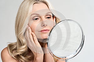 Closeup portrait middle age 50 woman looking at mirror, touching healthy skin. photo