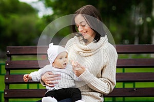 Closeup portrait of mom playing with baby outdoors at bench at park background