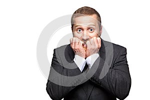 Closeup portrait of nervous handsome businessman with facial beard in black suit standing, biting his nails and looking at camera