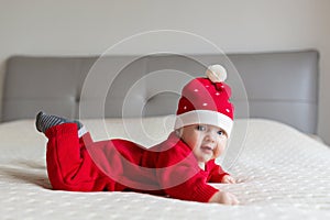 Closeup portrait of newborn baby. Cute Caucasian baby girl 3-4 months old in Santa costume lying on knitted cozy blanket on bed.