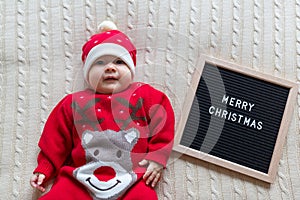 Closeup portrait of newborn baby. Cute Caucasian baby girl 3-4 months old in Santa costume lying on knitted cozy blanket on bed.