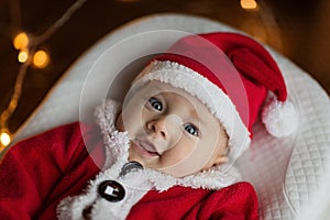 Closeup portrait of newborn baby. Cute Caucasian baby girl 4-5 months old in Santa costume lying on knitted cozy blanket