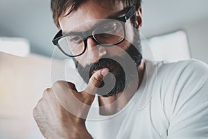 Closeup portrait of pensive bearded designer wearing eye glasses and working at the modern lightful office loft