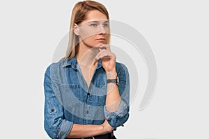 Closeup portrait of pensive beautiful young woman in denim shirt with finger folded frowning her face and looking to the one side