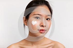 Closeup portrait of pretty korean lady with moisturizer cream on her face in heart shape, white studio background
