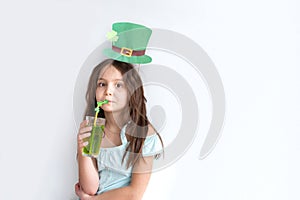 Closeup portrait of a pretty preteen caucasian girl in an emerald leprechaun hat with glass of green drink with a straw decorated