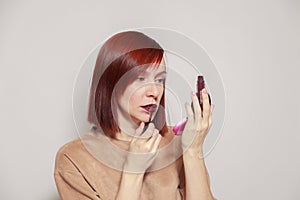 Closeup portrait redhead beautiful girl looking in mirror compact powder and paints lips with dark burgundy purple liquid lipstick