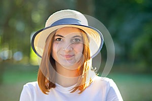 Closeup portrait of redhead hipster teenage girl in yellow hat smiling outdoors in sunny summer park