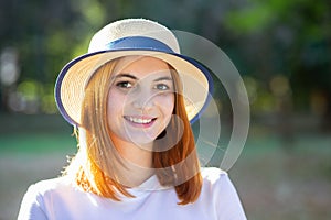 Closeup portrait of redhead hipster teenage girl in yellow hat smiling outdoors in sunny summer park