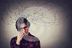 Closeup portrait of sad and thoughtful teen guy, hand under cheek, looking down feel headache, isolated on grey wall. Upset boy