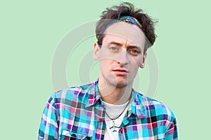 Closeup portrait of sad tired young man in casual blue checkered shirt and headband standing and looking at camera with sadness on