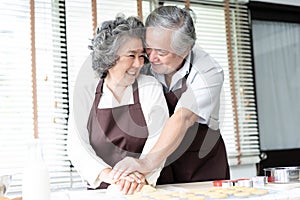 Closeup Portrait of senior Asian couple wearing aprons and smiling while mixing the dough while cooking togethe at the kitchen.