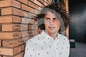 Closeup portrait of serious handsome Caucasian male model with curly hair and freckles, wears trendy shirt, posing on outdoor