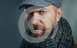 Closeup portrait of serious man with beard in cap and scarf. Winter accessories. Handsome bearded man in gray scarf and