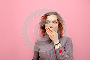 Closeup portrait of shocked attractive girl with curly hair covering mouth with her hand and looking away with frightened face