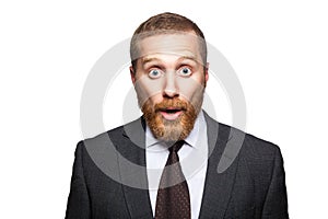 Closeup portrait of shocked handsome businessman with facial beard in black suit standing and looking at camera with big eyes and