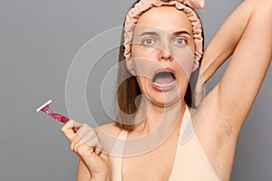Closeup portrait of shocked scared frighten woman shaving armpit with pink shaver isolated on gray background, raised arm,