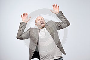 Closeup portrait of shocked stunned surprised mature man in casual suit, hands in air yelling and screaming or shouting