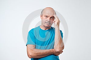 Closeup portrait of sleepy mature man in blue t-shirt, funny guy placing head on hand, unhappy looking at camera.