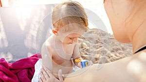Closeup portrait of smiling 3 years old toddler boy relaxing on the sea beach with young mother. CHild applying